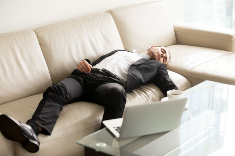 Worker sleeping on sofa with laptop in front ot him